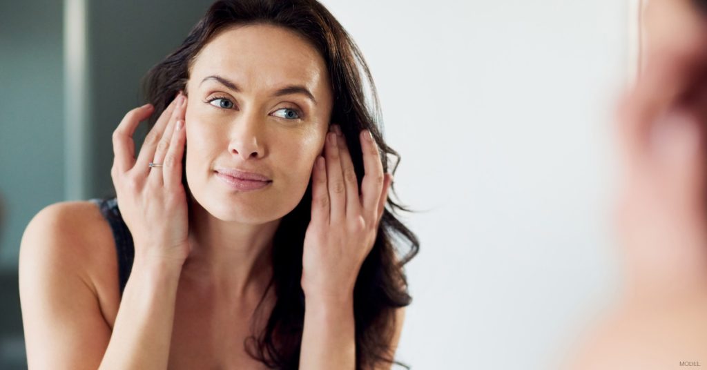 Woman looking at skin in mirror after laser skin resurfacing treatment in Atlanta, Georgia