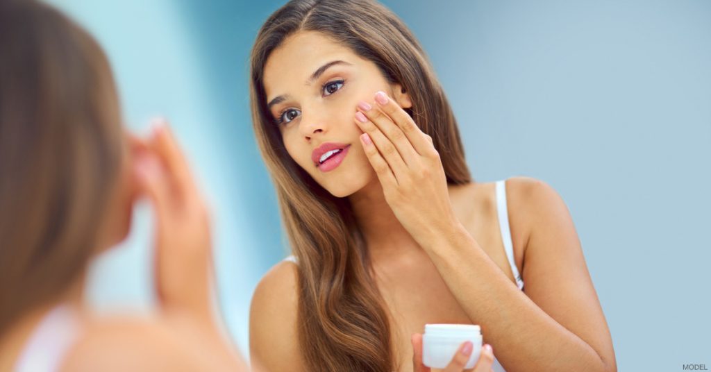 Woman putting on face cream in mirror