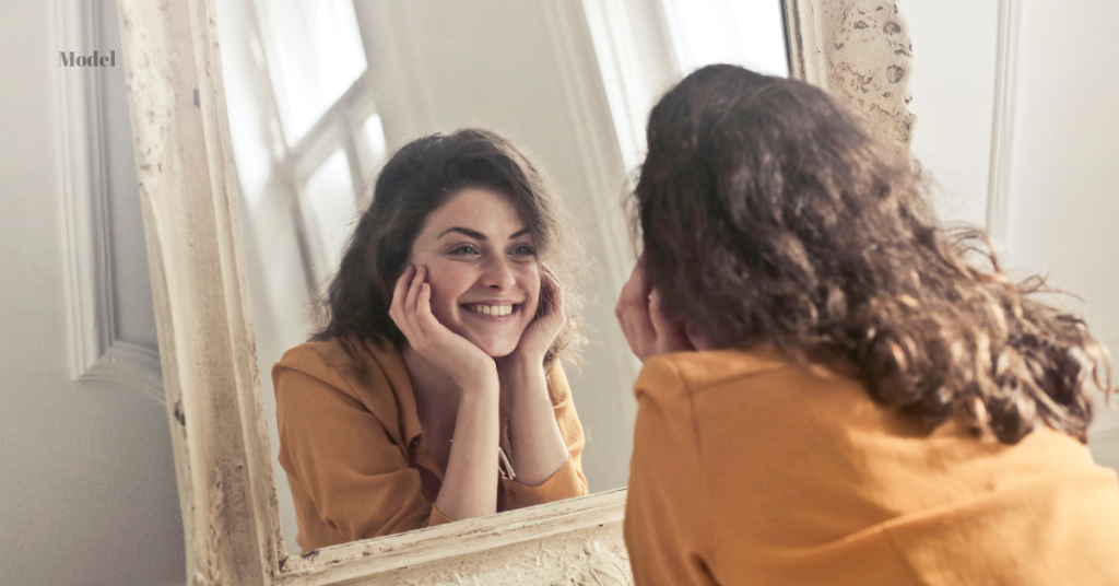 woman looking in the mirror and enjoying refreshed skin after laser skin treatment (model)